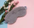 Close-up of a soft grey plush eye mask for comfortable sleep with decorative roses background - Gray