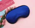 Close-up of silky blue sleep eye mask with soft blackout fabric on pink background - Sapphire Blue