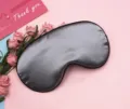 Detailed view of soft silver satin sleep mask with elegant black piping on pink background. - Gray
