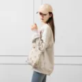 Vue de profil d'un sac cabas en velours côtelé à motifs souriants porté par un mannequin - Nouveau sac à main en velours côtelé beige avec smiley