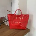 Vibrant red glossy PVC tote bag with laser-cut flower patterns and white lettering. - Red