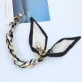 Λεπτομέρεια χειροποίητης αλυσίδας από μετάξι με χρυσά κουμπώματα σε λευκό φόντο - Γράμμα με Μαύρο Περίγραμμα