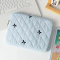 Light blue quilted laptop sleeve with black embroidered bow pattern on a white desk. - 13" / Light Blue