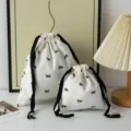 Two sweet white drawstring storage bags with black bow patterns for desktop organization - Black