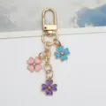 Close-up detail of a gold alloy keychain with three colorful enamel flower charms - Blue Pink Purple