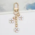 Detailed view of a gold alloy keychain with three white enamel clover pendants and rhinestones - White