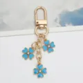 Close-up detail of a gold alloy keychain with three light blue enamel flower charms - Lake Blue