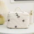Cream quilted cosmetic bag with black embroidered bows displayed in a lifestyle setting - 23*16*16cm / Beige
