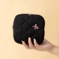 Detailopname van zwart gewatteerd tasje met roze strikborduursel in de hand. - 12.5*5*12.5cm / Zwart