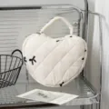 Gesteppte herzförmige Handtasche mit Schleifenstickerei auf Regal - Beiger Stoff mit Bestickter Schleife
