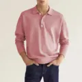 Gedetailleerd overzicht van een stijlvol roze polo met lange mouwen, knoopkraag en fijne textuur. - Roze