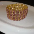 Detailansicht eines breiten, goldenen, mehrreihigen Stretcharmbands mit glänzenden rosa Strasssteinen. - Rosa
