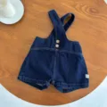 Infant denim overalls detail view, showing cross straps, metal buttons, and size tag. - 73cm / Dark Blue Suspenders