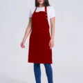 Detail view of the red bib apron featuring adjustable neck straps, buttons, and front utility pockets. - Burgundy