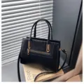 Elegante bolso de mano negro con panel de textura de cocodrilo, detalles dorados y correa práctica. - Negro