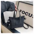 Vue détaillée d'un sac cabas en toile noire, avec doubles poignées et bandoulière réglable. - Noir