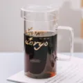 Heldere glazen koffiemok met deksel en gouden opdruk, minimalistische stijl voor thuis. - Gouden letters model + glazen deksel