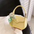 Elegante blassgelbe Nischen-Design-Handtasche mit einer dekorativen grünen Blumenschleife - Gelb