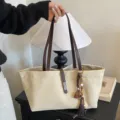 Bolso tote grande de lona beige con correas de cuero marrón y un colgante de borla decorativo - Con Colgante / Blanco Roto