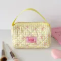 Detailweergave van een geel geruite gewatteerde make-uptas met roze stoffen patch. - Geel