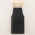Black cotton twill work apron with brown straps and front pocket for cooking coffee. - Black