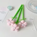 Macro view of three pink fabric flower gel pens with green stems on white background - Pink