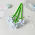 Close-up of three decorative gel pens with light blue fabric flowers and green stems - Blue