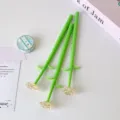 Detail view of green flower-shaped pens with amber crystal rose tips on white desk. - Beige