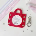 Red handbag-shaped badge holder with a circular display window and metal clasp pendant - Including Four Ribbons in Two Colors / Red