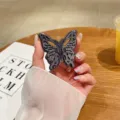 Detaillierter Schuss eines hohlen Schmetterlings-Handyhalters aus Metall mit kreativem 3D-Design. - Schwarz