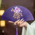 Chinese style purple bamboo folding fan with hollow carved design, peony painting and tassel. - Purple Rhyme Peony