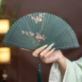 Traditional Chinese folding bamboo fan with hollow carved design and plum blossom pattern - Green Blooming Red Plum