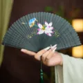 Traditional Chinese bamboo folding hand fan with carved hollow design, lotus and green tassel. - Green Lotus Fragrance