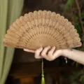 Natural green sandalwood folding fan with elegant floral hollow carving and green tassel. - Qinghan Green Sandalwood