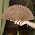 Handcrafted wooden folding fan with delicate carved lotus patterns and green tassel for traditional style. - Lotus Ripple Green Sandalwood