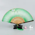 Traditional Chinese folding fan with green silk fabric, floral pattern, and wooden frame. - Floral Leaves / Green