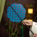 Traditional Chinese style folding round fan with blue fish scale pattern and green tassel. - 8-Petal Color-Changing Radish Waist Fan (Bamboo Edge)