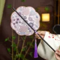 Traditional Chinese style embroidered round fan with bamboo handle and elegant purple tassel. - 8-Petal Hundred Flowers Waist Fan (Bamboo Edge)