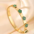 Detail shot of a luxury gold-tone titanium steel bangle featuring green striped flower motifs. - DQ-2441-1 (Clover Style)