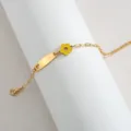 Detalle en primer plano de pulsera de acero dorado con flor esmaltada amarilla y placa lisa. - Corazón Hueco (Flor Amarilla) / Color acero