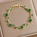 Close-up of elegant gold-tone vine bracelet sparkling with vibrant green cubic zirconia stones. - DQ-W-4092-4