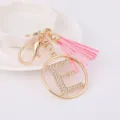 Detail shot of gold rhinestone letter E keychain charm with pink tassel and metal clasp. - Letter E