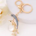 Gold dolphin keychain with blue rhinestones and pearl pendant, elegant metal bag charm detail. - Dolphin 13