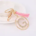 Close up of gold metal rhinestone letter G keychain pendant with pink tassel detail display. - Letter G