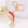 Chic gold-tone dolphin keychain featuring dazzling red rhinestones and a elegant white pearl pendant for bags. - Dolphin 15