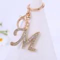 Close-up view of a sparkly rhinestone letter M keychain pendant with gold alloy hook and ring. - M