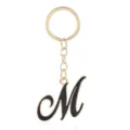 Close-up detail of the elegant gold-plated keychain featuring a black enamel letter M pendant. - Letter M