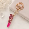 Porte-clés rouge à lèvres étincelant avec strass roses et finition dorée élégante. - Rose vif