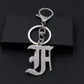 Detailed close-up shot of a silver rhinestone gothic alphabet letter keychain pendant. - Letter F