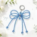 Sparkling blue crystal beaded bow bag charm detail with shiny silver clasp and dangling strands. - Blue